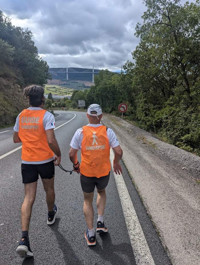 Les Cenbornards de Millau : récit de deux kinés déficients visuels qui ont défié les 100 km 1 Nicolas et son guide Erwan de dos sur les 100 km, face à eux : le viaduc de Millau